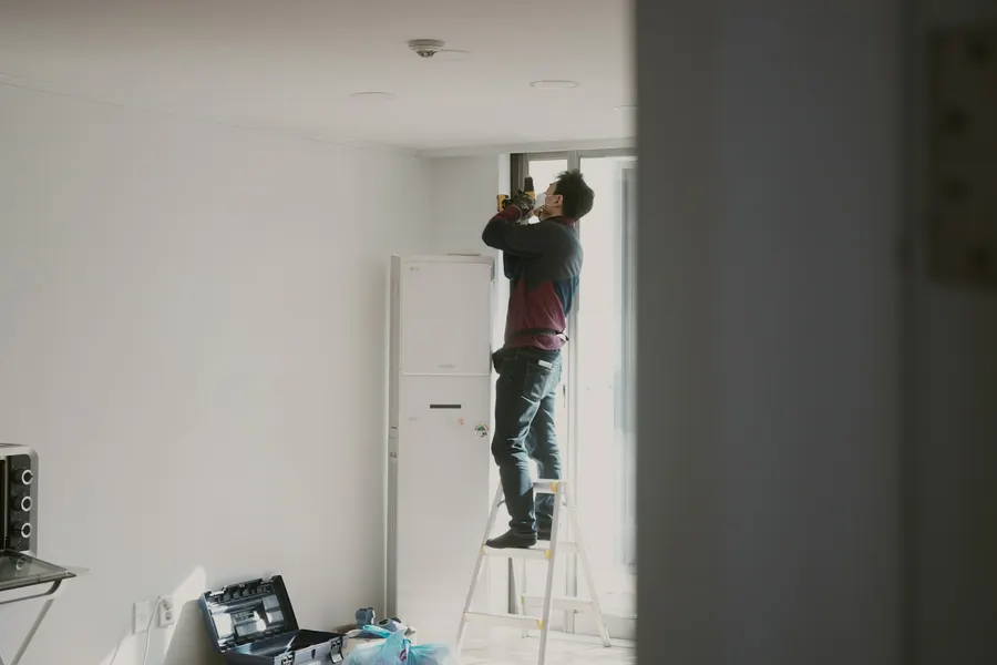 Hausmeister arbeitet auf der Leiter an einer Deckeninstallation