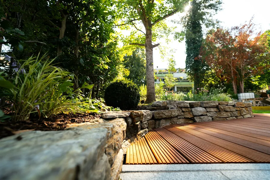 Terrasse mit Holzdeck und Natursteinmauer in einem gepflegten Garten
